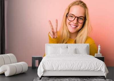 Adorable teenager woman showing victory sign and smiling broadly. Wall mural