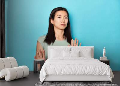 Asian woman in summer green top, studio backdrop, rejecting someone showing a gesture of disgust. Wall mural