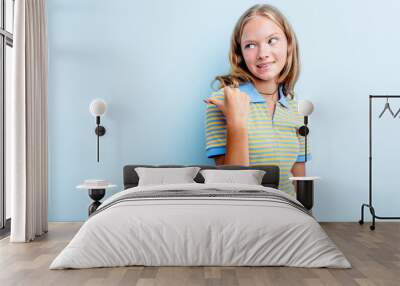 Caucasian teen girl isolated on blue background points with thumb finger away, laughing and carefree. Wall mural