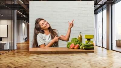 Concept of diet. Portrait of a healthy young latin woman pointing to the side, smiling surprised presenting something, natural and casual Wall mural