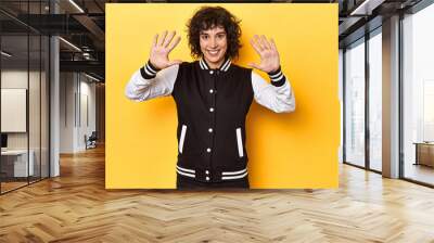 Curly-haired Caucasian woman in baseball jacket showing number ten with hands. Wall mural