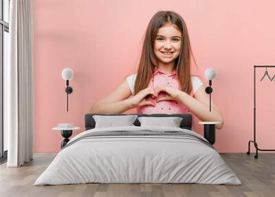 Cute little girl smiling and showing a heart shape with him hands. Wall mural