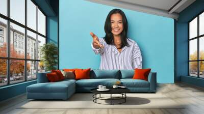 Filipina young woman on blue studio stretching hand at camera in greeting gesture. Wall mural