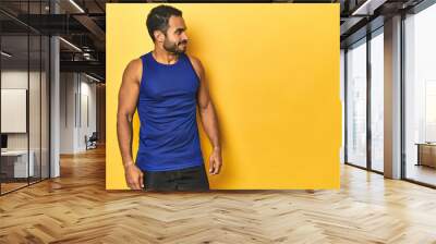 Fit Latino man in sportswear pointing to space, yellow studio background. Wall mural