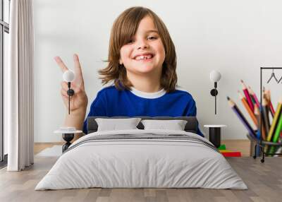 Little boy painting and doing homeworks on his desk joyful and carefree showing a peace symbol with fingers. Wall mural