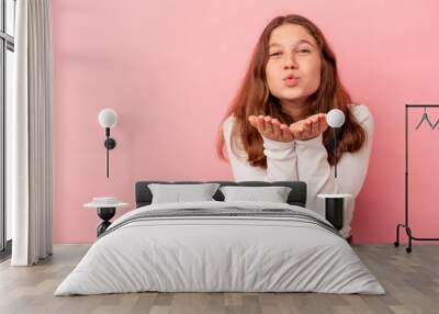 Little caucasian girl isolated on pink background folding lips and holding palms to send air kiss. Wall mural