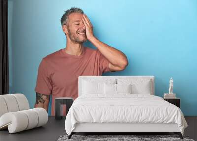 Middle-aged caucasian man on blue backdrop laughing happy, carefree, natural emotion. Wall mural