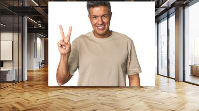 Middle-aged Latino man joyful and carefree showing a peace symbol with fingers. Wall mural