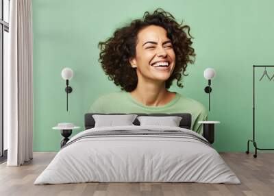 Portrait of happy young woman laughing and looking at camera over green background Wall mural