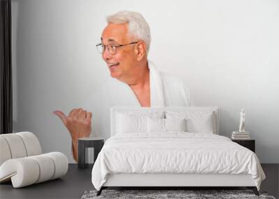 Senior american man wearing bathrobe isolated on white background points with thumb finger away, laughing and carefree. Wall mural