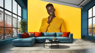 Stylish young African man on vibrant yellow studio background, smiling happy and confident, touching chin with hand. Wall mural