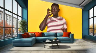 Stylish young African man on vibrant yellow studio background, with fingers on lips keeping a secret. Wall mural