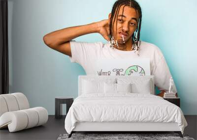 Young African American man holding protect our planet placard isolated on blue background touching back of head, thinking and making a choice. Wall mural