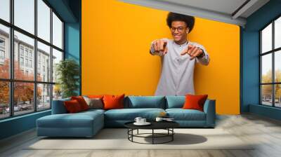 Young african american man over an orange wall cheerful and smiling pointing to front Wall mural