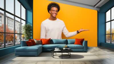 Young african american man over an orange wall holding something with hand Wall mural