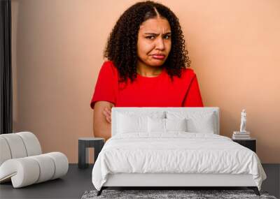 Young African American woman isolated on beige background frowning face in displeasure, keeps arms folded. Wall mural