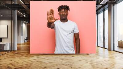 Young african black man standing with outstretched hand showing stop sign, preventing you. Wall mural