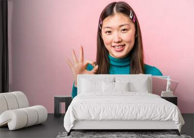 Young asian student woman holding books isolated on pink background cheerful and confident showing ok gesture. Wall mural