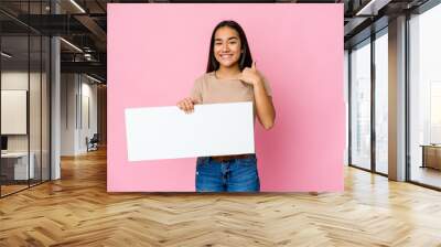 Young asian woman holding a blank paper for white something over isolated background showing a mobile phone call gesture with fingers. Wall mural