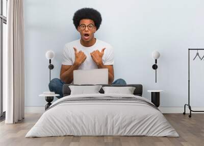 Young black man sitting on the floor with a laptop surprised, feels successful and prosperous Wall mural