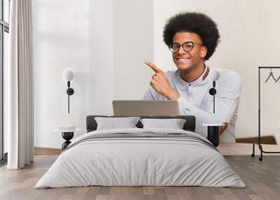 Young black man using his laptop smiling and pointing to the side Wall mural