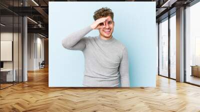 Young blond curly hair caucasian man isolated excited keeping ok gesture on eye. Wall mural