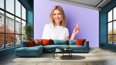 Young blonde caucasian woman isolated smiling cheerfully pointing with forefinger away. Wall mural