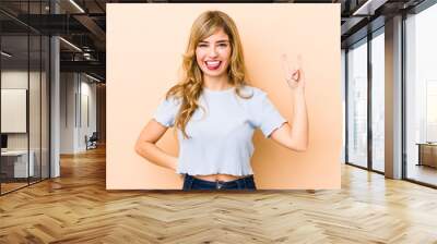 Young blonde caucasian woman showing rock gesture with fingers Wall mural