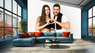 Young caucasian fitness couple isolated smiling and showing a heart shape with hands. Wall mural