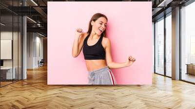 Young caucasian fitness woman posing in a pink background dancing and having fun. Wall mural