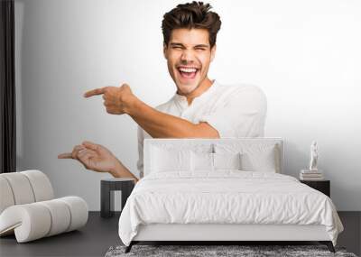 Young caucasian handsome man isolated excited pointing with forefingers away. Wall mural