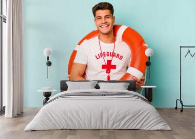 Young caucasian lifeguard isolated on blue background happy, smiling and cheerful. Wall mural