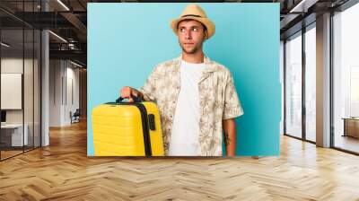 Young caucasian man going to travel isolated on blue background  confused, feels doubtful and unsure. Wall mural