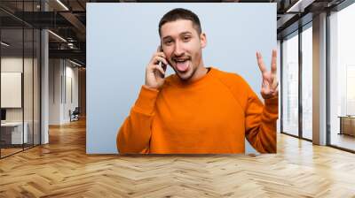 Young caucasian man holding a phone showing number two with fingers. Wall mural