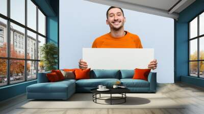 Young caucasian man holding a placard happy, smiling and cheerful. Wall mural