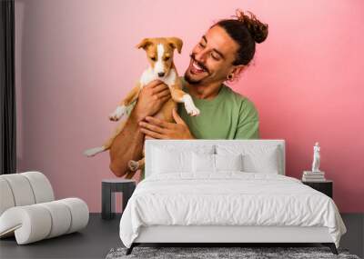 Young caucasian man holding his puppy isolated on pink background Wall mural