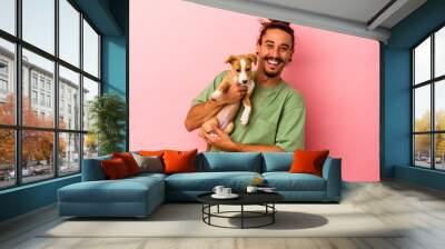 Young caucasian man holding his puppy isolated on pink background Wall mural