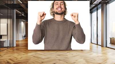 Young Caucasian man in studio setting celebrating a victory, passion and enthusiasm, happy expression. Wall mural