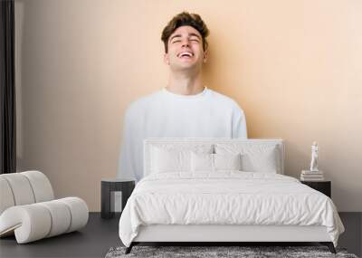 Young caucasian man isolated on beige background relaxed and happy laughing, neck stretched showing teeth. Wall mural