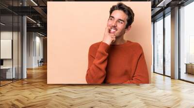 Young caucasian man isolated on beige background relaxed thinking about something looking at a copy space. Wall mural