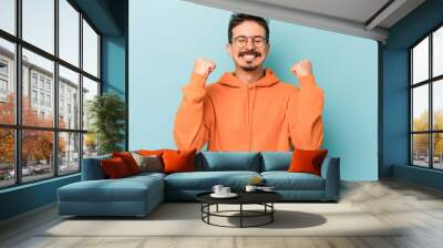 Young caucasian man isolated on blue background celebrating a victory, passion and enthusiasm, happy expression. Wall mural