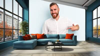 Young caucasian man isolated on blue background person pointing by hand to a shirt copy space, proud and confident Wall mural