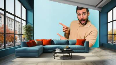 Young caucasian man isolated on blue background pointing with forefingers to a copy space, expressing excitement and desire. Wall mural