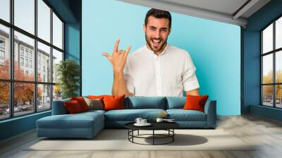 Young caucasian man isolated on blue background showing rock gesture with fingers Wall mural