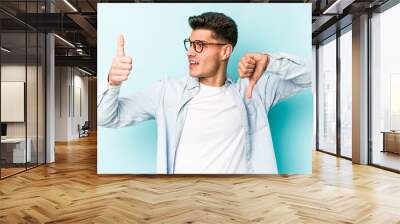 Young caucasian man isolated on blue background showing thumbs up and thumbs down, difficult choose concept Wall mural