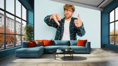 Young caucasian man isolated on blue background showing thumbs up and thumbs down, difficult choose concept Wall mural