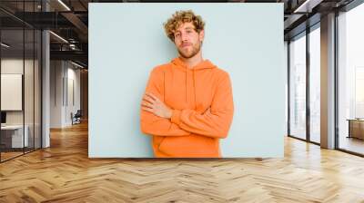 Young caucasian man isolated on blue background who feels confident, crossing arms with determination. Wall mural