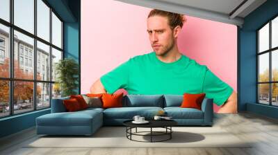 Young caucasian man isolated on pink background frowning face in displeasure, keeps arms folded. Wall mural