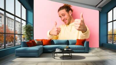 Young caucasian man isolated on pink background raising both thumbs up, smiling and confident. Wall mural