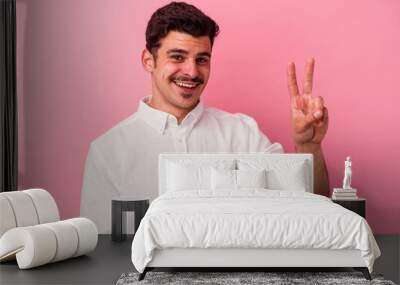 Young caucasian man isolated on pink background showing victory sign and smiling broadly. Wall mural